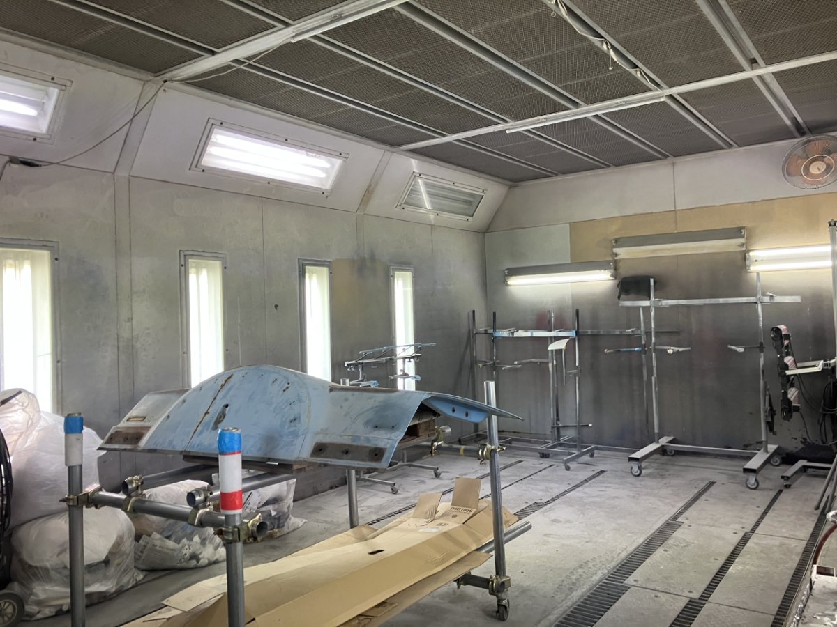 自動車修理工場の塗装ブースで青い車体部品が作業台に置かれている様子