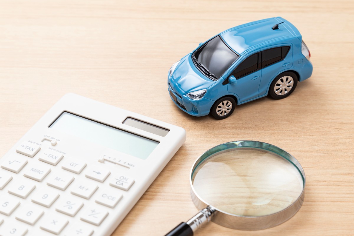 木製テーブル上の青い車の模型と電卓と虫眼鏡